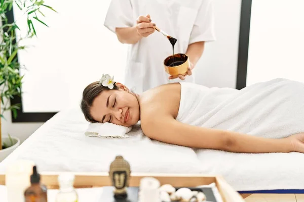 Young latin woman relaxed having back massage with chocolate therapy at beauty center