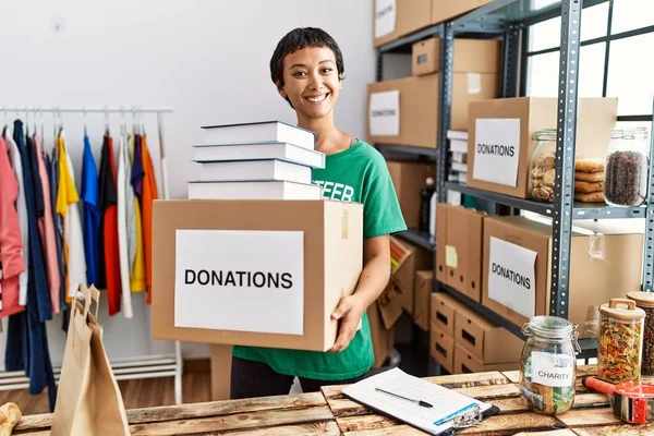 Young Hispanic Woman Wearing Volunteer Uniform Holding Books Donations Package — Stock Photo, Image