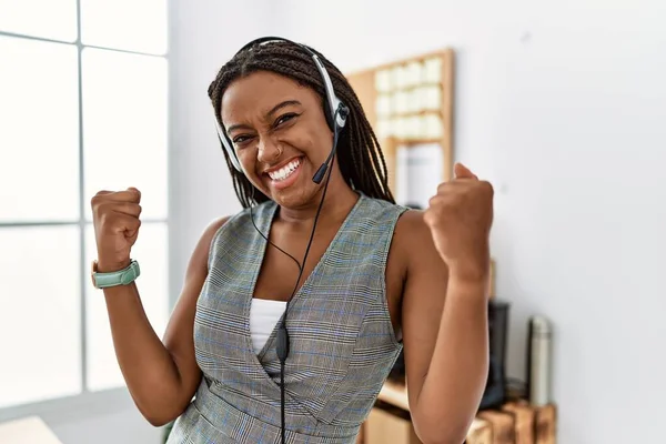 Young african american woman working at the office wearing operator headset very happy and excited doing winner gesture with arms raised, smiling and screaming for success. celebration concept.