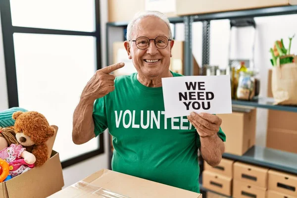 Senior volunteer man holding we need you banner pointing finger to one self smiling happy and proud