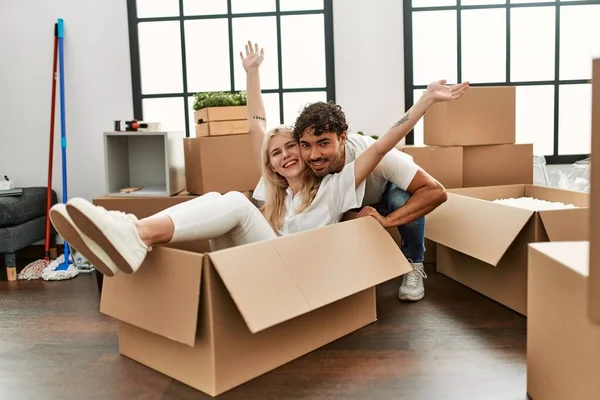 Young beautiful couple smiling happy playing using cardboard box as a car at new home.