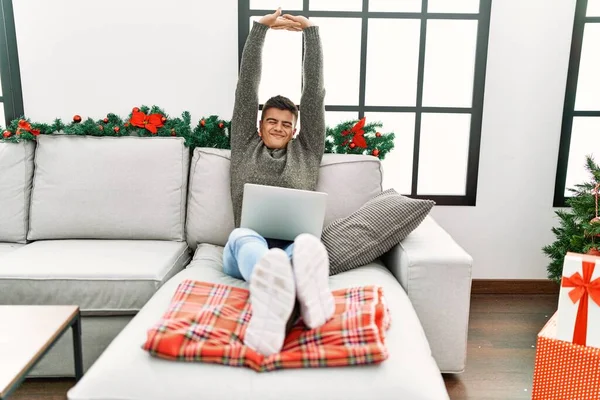 Young Hispanic Man Stretching Arms Using Laptop Sitting Sofa Christmas — 스톡 사진