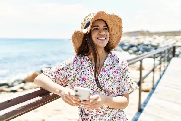 若いですラテン語の女の子身に着けています夏の帽子を使用してスマートフォンでビーチ — ストック写真