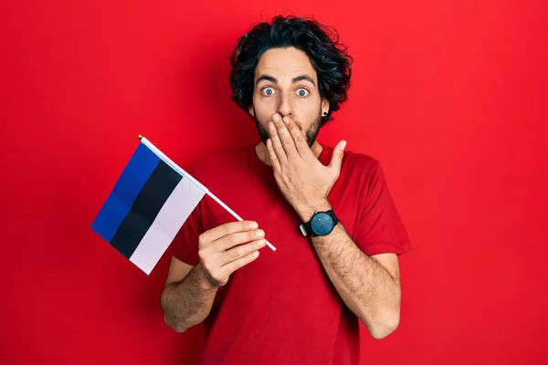 Pohledný Hispánec Držící Estonskou Vlajku Ústech Šokovaný Vystrašený Omylu Překvapený — Stock fotografie