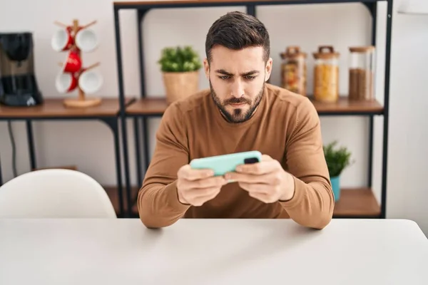 Hombre Hispano Joven Usando Teléfono Inteligente Sentado Mesa Casa —  Fotos de Stock