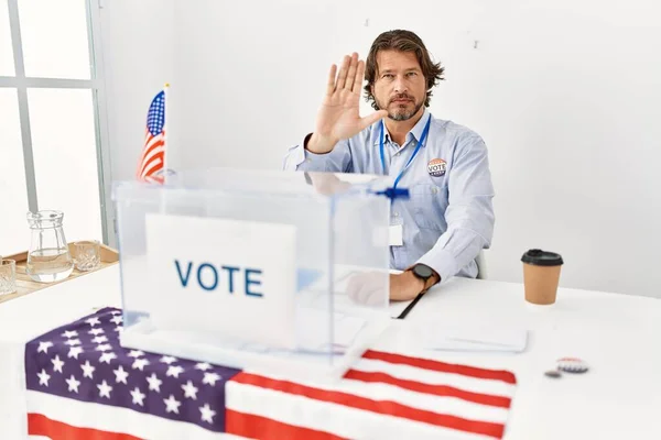 一个英俊的中年男人坐在投票站里 手牵着手唱着歌 用消极而严肃的手势警告人 — 图库照片