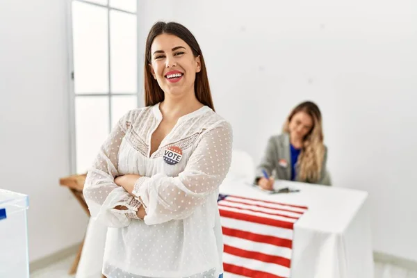 Young american voter woman wearing i voted badge standing with arms crossed gesture at electoral college.