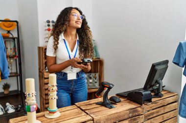 Genç Latin esnaf mağazasında veri telefonu kullanarak mutlu bir şekilde gülümsüyor..