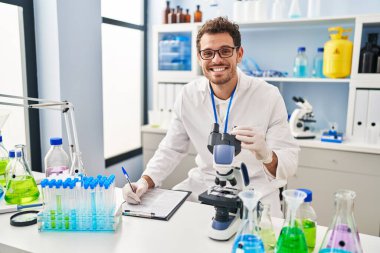 Genç İspanyol bilim adamı, laboratuarda mikroskop kullanarak belgeye yazı yazıyor.