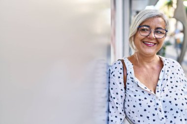 Orta yaşlı bir kadın sokakta kendine güvenerek gülümsüyor.