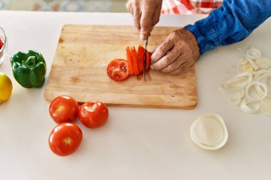 Kıdemli adam mutfakta domates kesiyor.