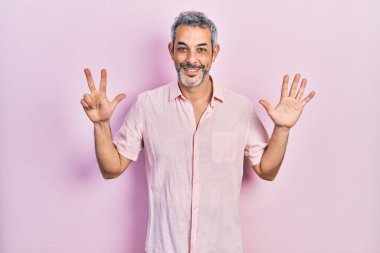 Yakışıklı, orta yaşlı, gri saçlı, sıradan tişörtlü, 8 numaralı parmaklarıyla gösteriş yapan, kendinden emin ve mutlu bir adam.. 