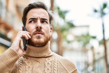 Ciddi bir suratı olan beyaz bir genç şehirde akıllı telefondan konuşuyor..