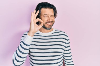 Orta yaşlı, günlük kıyafetler giyen, gülümseyen beyaz bir adam el ve parmaklarıyla 