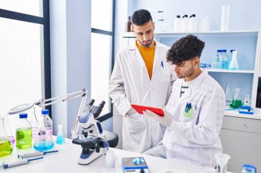 Laboratuvarda çalışan iki bilim adamı dokunmatik ped kullanıyor.