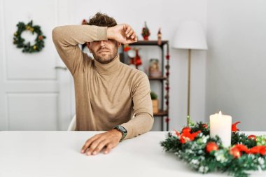 Masaya sakallı genç yakışıklı bir adam oturuyor. Yılbaşı süslemeleriyle gözlerini kollarıyla kapatıyor, ciddi ve üzgün görünüyor. Görme, saklama ve reddetme konsepti 