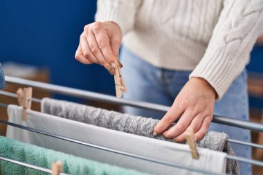 Çamaşır odasında çamaşır ipine elbise asan genç bir kadın.