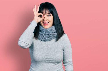 Latin kökenli genç ve uzun boylu bir kadın. Kış eşarbı takıyor. El hareketleriyle gülümsüyor.. 