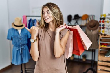 Alışveriş torbalarını elinde tutan genç sarışın kadın mutlu yüzle gülümseyen ve başparmağıyla yan tarafı gösteren.. 