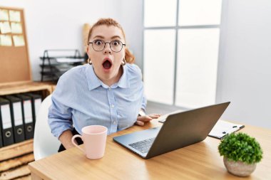 Ofiste çalışan genç kızıl saçlı kadın bilgisayarlı dizüstü bilgisayar kullanıyor. Şaşırmış ve şaşırmış bir ifade, korku ve heyecanlı bir yüz ifadesi var.. 