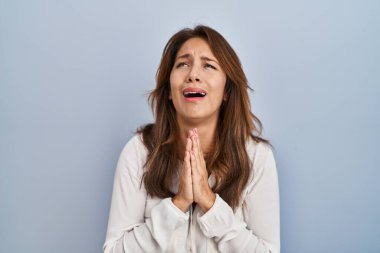 Hispanik kadın, izole edilmiş arka planda duruyor. Elleriyle yalvarıyor ve dua ediyor. Yüzünde umut ifadesi var. Çok duygusal ve endişeli. Yalvarıyor. 
