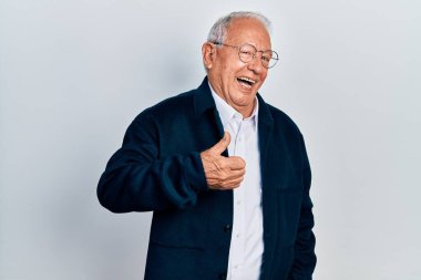 Gri saçlı, sıradan giyinen ve gözlüklü yaşlı adam el hareketleriyle mutlu baş parmaklar yapıyor. Kameraya bakıp başarıyı gösteren ifade. 