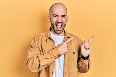 Genç kel adam, günlük giysiler içinde gülümsüyor ve kameraya bakıyor. İki eliyle ve parmaklarıyla onu işaret ediyor.. 