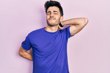 Günlük tişört giyen, boynu ağrıyan, eliyle boynuna dokunan, kasları ağrıyan genç bir İspanyol. 