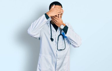 Doktor üniforması giyen genç Afro-Amerikalı adam ve steteskop gözleri ve ağzı ellerle kapatıyor, şaşırmış ve şok olmuş. duygu gizleme 