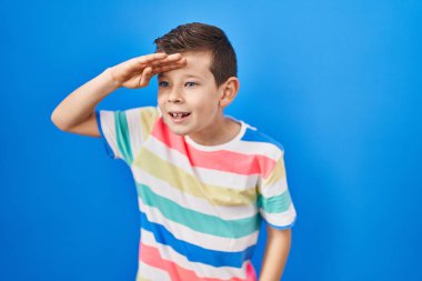 Mavi arka planda dikilen beyaz çocuk çok mutlu ve gülümsüyor. arama kavramı. 