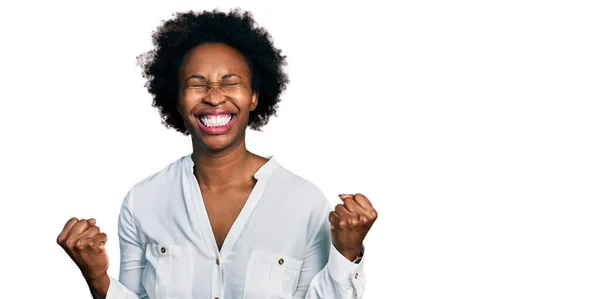 黑头发的非洲裔美国女人穿着休闲的白色T恤 非常高兴而兴奋地举起双臂做着获胜的手势 微笑着 尖叫着要成功 庆祝概念 — 图库照片
