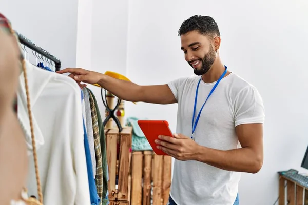年轻的阿拉伯男子店主用触摸板站在服装店的衣架旁 — 图库照片