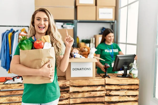 Mujer Rubia Joven Centro Voluntarios Sosteniendo Donaciones Caja Papel Sorprendida —  Fotos de Stock