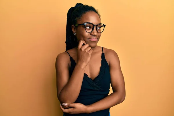 African american woman with braided hair wearing casual clothes and glasses thinking concentrated about doubt with finger on chin and looking up wondering