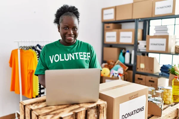在慈善中心工作的身穿志愿制服的年轻非洲裔美国妇女使用笔记本电脑 — 图库照片