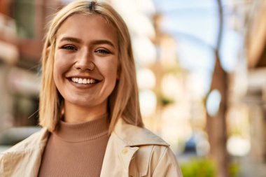 Genç sarışın kız gülümsüyor, mutlu bir şekilde şehirde duruyor..