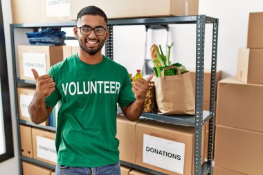Genç Hintli gönüllü bağış kutusu başarı işareti tutuyor. Elleriyle olumlu jest yapıyor. Gülümsüyor ve mutlu. Neşeli ifade ve kazanan jest. 