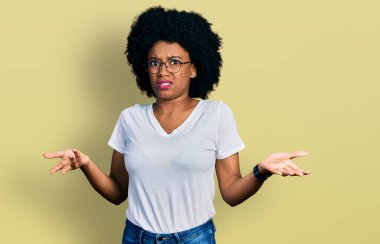 Gündelik beyaz tişört giyen genç Afrikalı Amerikalı kadın. Hiçbir şeyden habersiz ve kolları açık, hiçbir fikri yok.. 