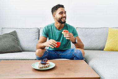 Genç Arap adam kahvaltısını evde, kanepede yapıyor.