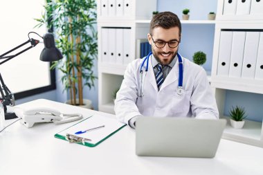 Klinikte çalışan dizüstü bilgisayar kullanan doktor üniforması giyen genç bir İspanyol.