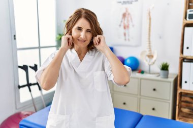 Orta yaşlı fizyoterapist kadın yüksek sesli müzik sesi için kulakları parmaklarıyla kapatıyor. sağır kavramı. 