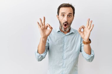 Arka planda sakallı, orta yaşlı, ispanyol bir adam. Şaşırmış ve şok olmuş görünüyor. Parmaklarıyla onay sembolü yapıyor. çılgın ifade 