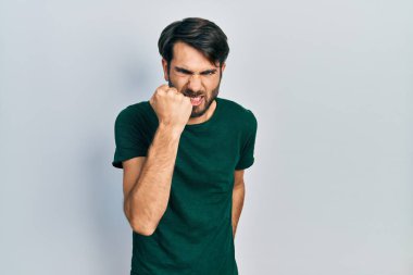 Genç, Latin asıllı, günlük beyaz tişört giyen kızgın ve kızgın yumruk kaldıran sinirli ve öfkeyle bağıran bir adam. öfke ve agresif konsept. 