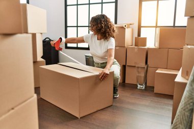 Orta yaşlı İspanyol kadın yeni evinde karton kutu paketlerken kendine güler.