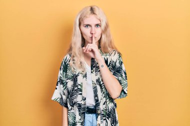 Beautiful caucasian woman with blond hair wearing tropical shirt asking to be quiet with finger on lips. silence and secret concept. 