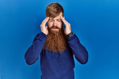 Kızıl saçlı, uzun sakallı mavi süveter giyen, elleri kafasında, stresten dolayı baş ağrısı çeken bir adam. migren ağrısı. 