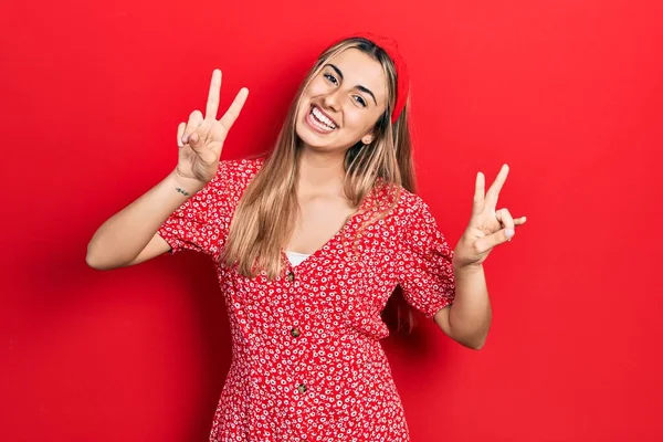 Yaz elbisesi giymiş, gülümseyen, parmaklarını zafer işareti yaparken gösteren güzel İspanyol kadın. İki numara.. 