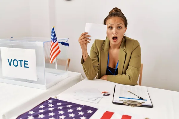 投票箱の中で投票を保持する美しいヒスパニック系の女性は怖がって驚きのために口を開けて驚いて 不信の顔 — ストック写真