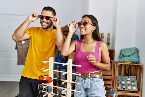 Genç Latin çift gülümseyerek mağazadan güneş gözlüğü seçiyor..