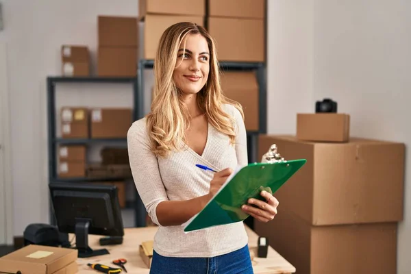 Young blonde woman ecommerce business worker writing on clipboard at office